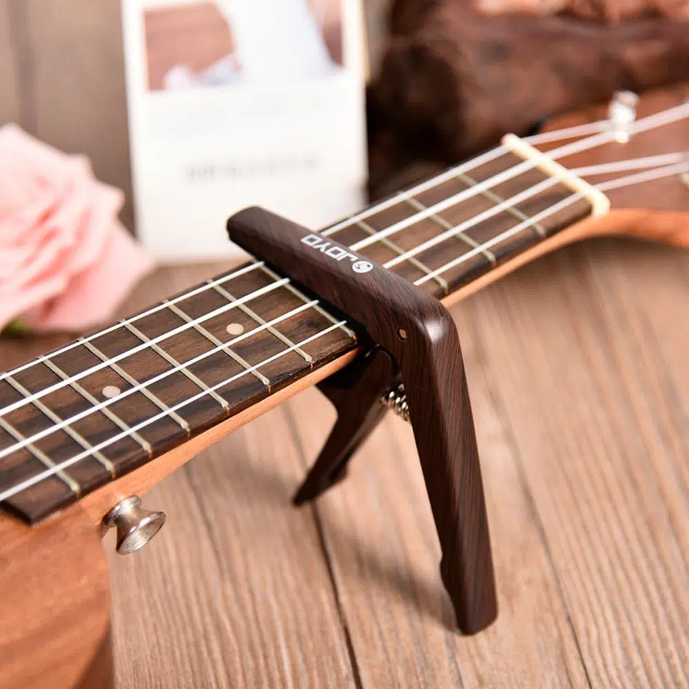 ukulele capo in wood clamped on ukulele fretboard