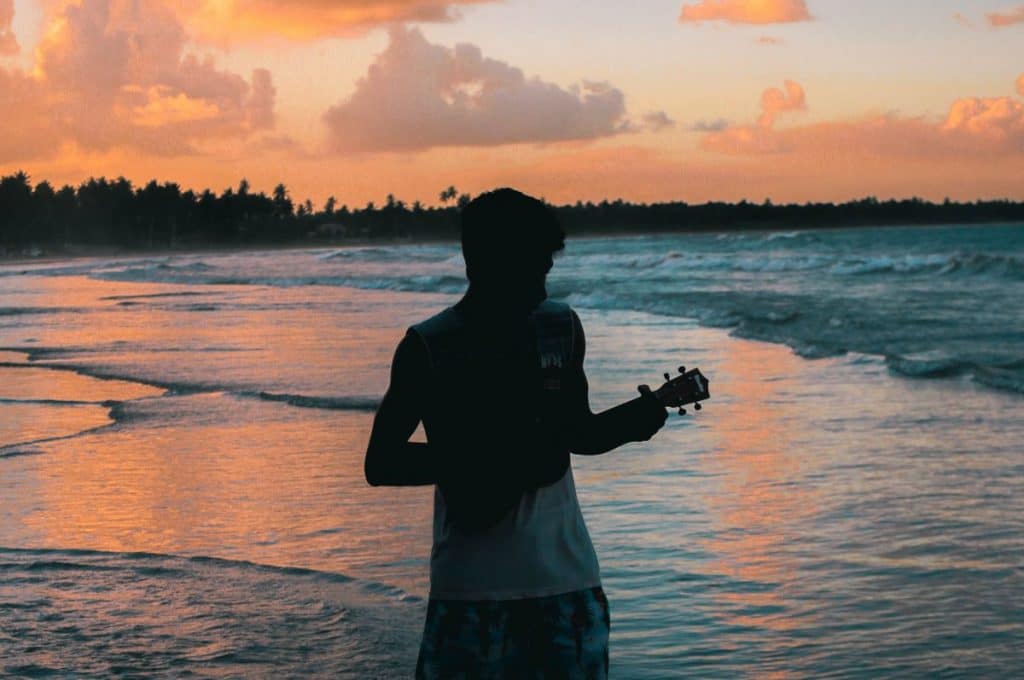 man playing the ukulele on the beach with the sea